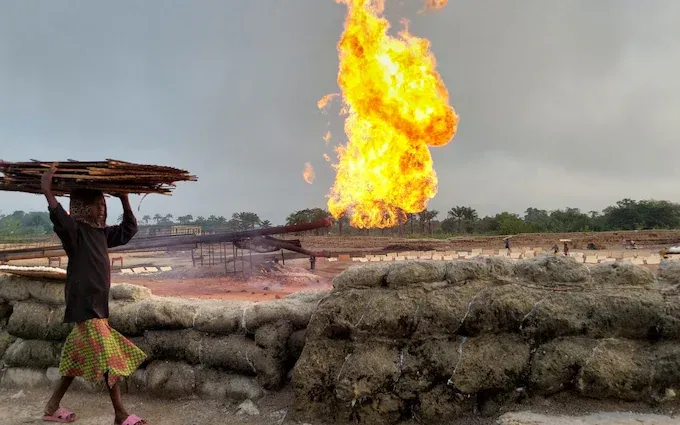 African woman walking with gas flaring fires behind herr